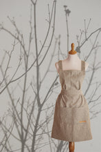 Load image into Gallery viewer, Blue striped apron in front of branches.